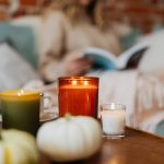 Why We Still Light Candles in a World Full of Screens Warm autumn scene with candles, pumpkins, and a person reading in a cozy setting.