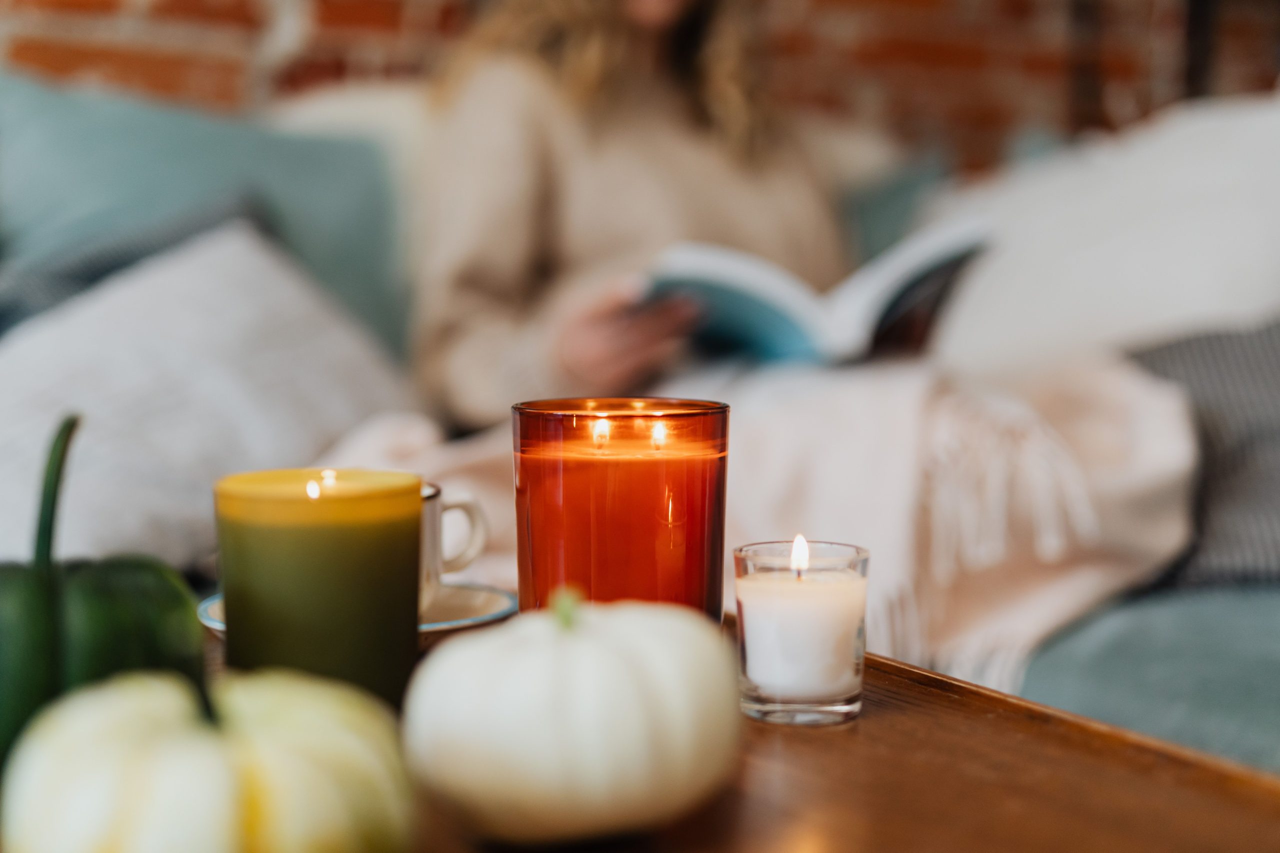 Why We Still Light Candles in a World Full of Screens Warm autumn scene with candles, pumpkins, and a person reading in a cozy setting.