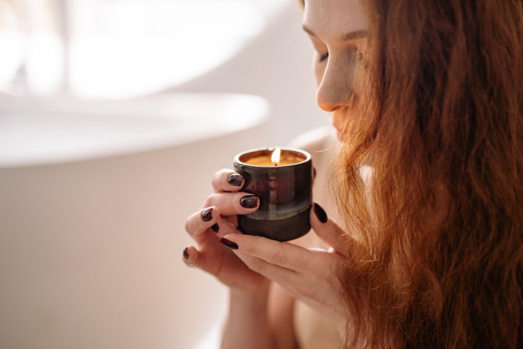 Woman enjoying the scent of a fragrant candle in a serene indoor setting.