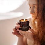 How to Choose a Candle Scent for Every Mood Woman enjoying the scent of a fragrant candle in a serene indoor setting.